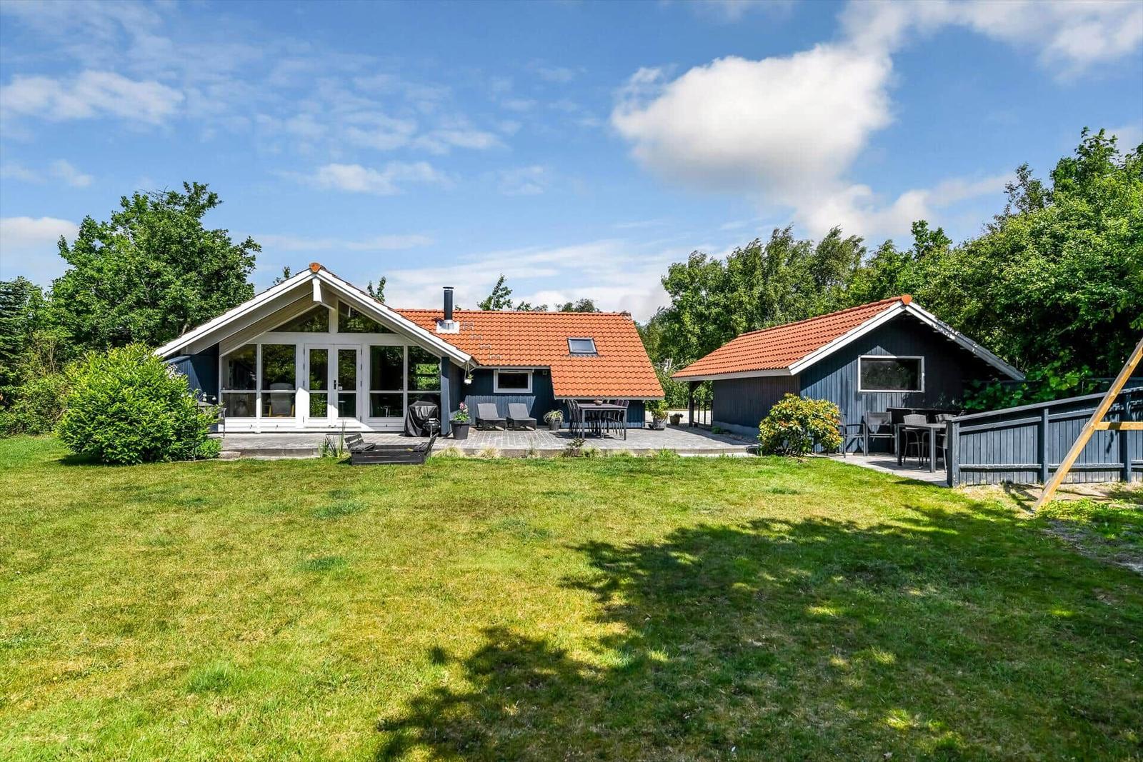 Zwei Häuser mit Terrassen und Garten unter blauem Himmel.