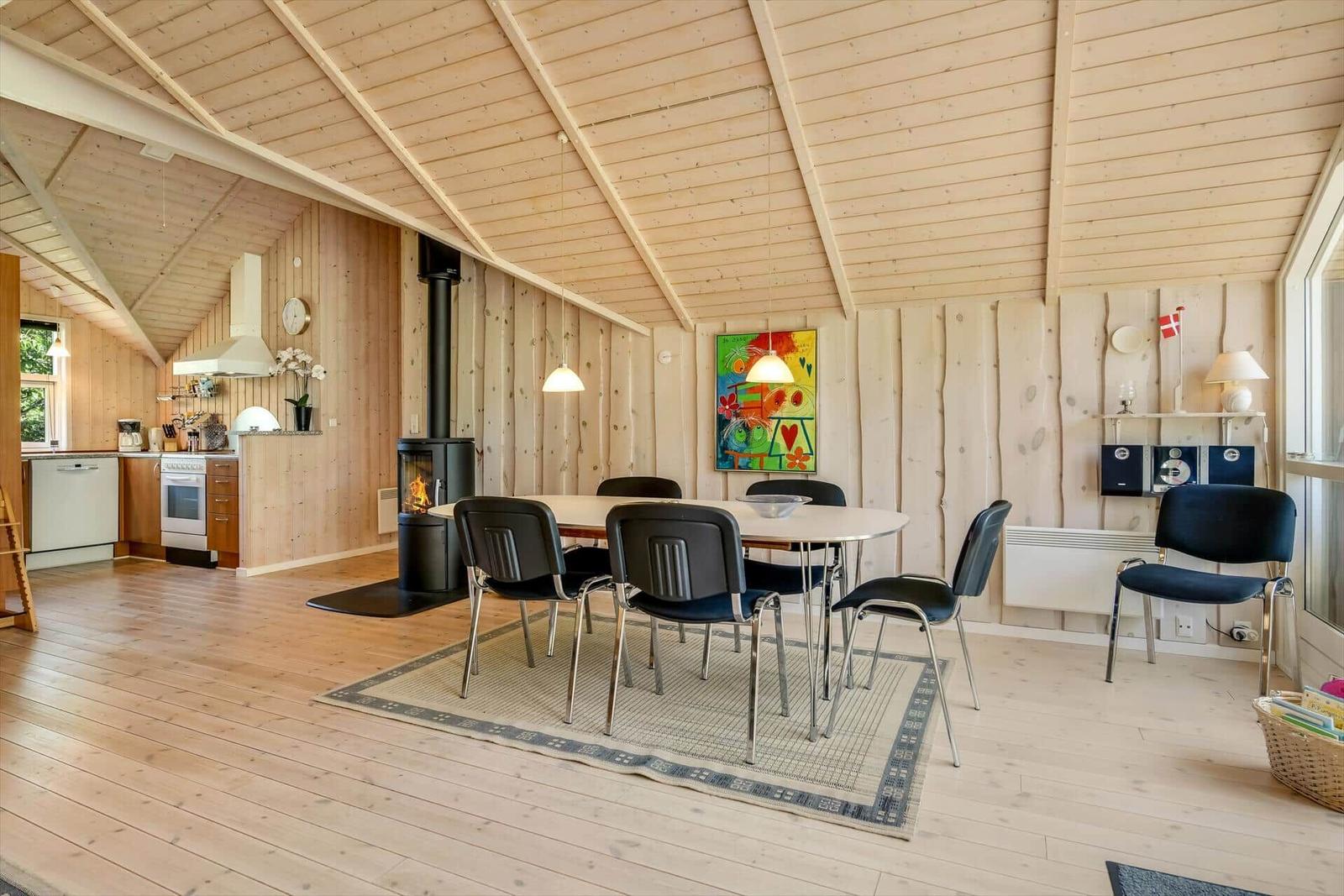 Essbereich mit Tisch, Stühlen und Kaminofen. Küche und Wohnbereich mit Holzwänden.