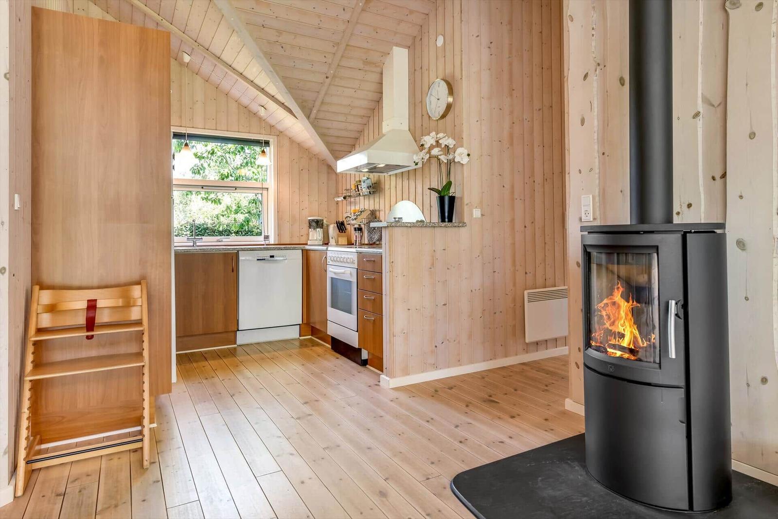Küche mit Holzwand und Kaminofen, Fensterblick auf Grün.