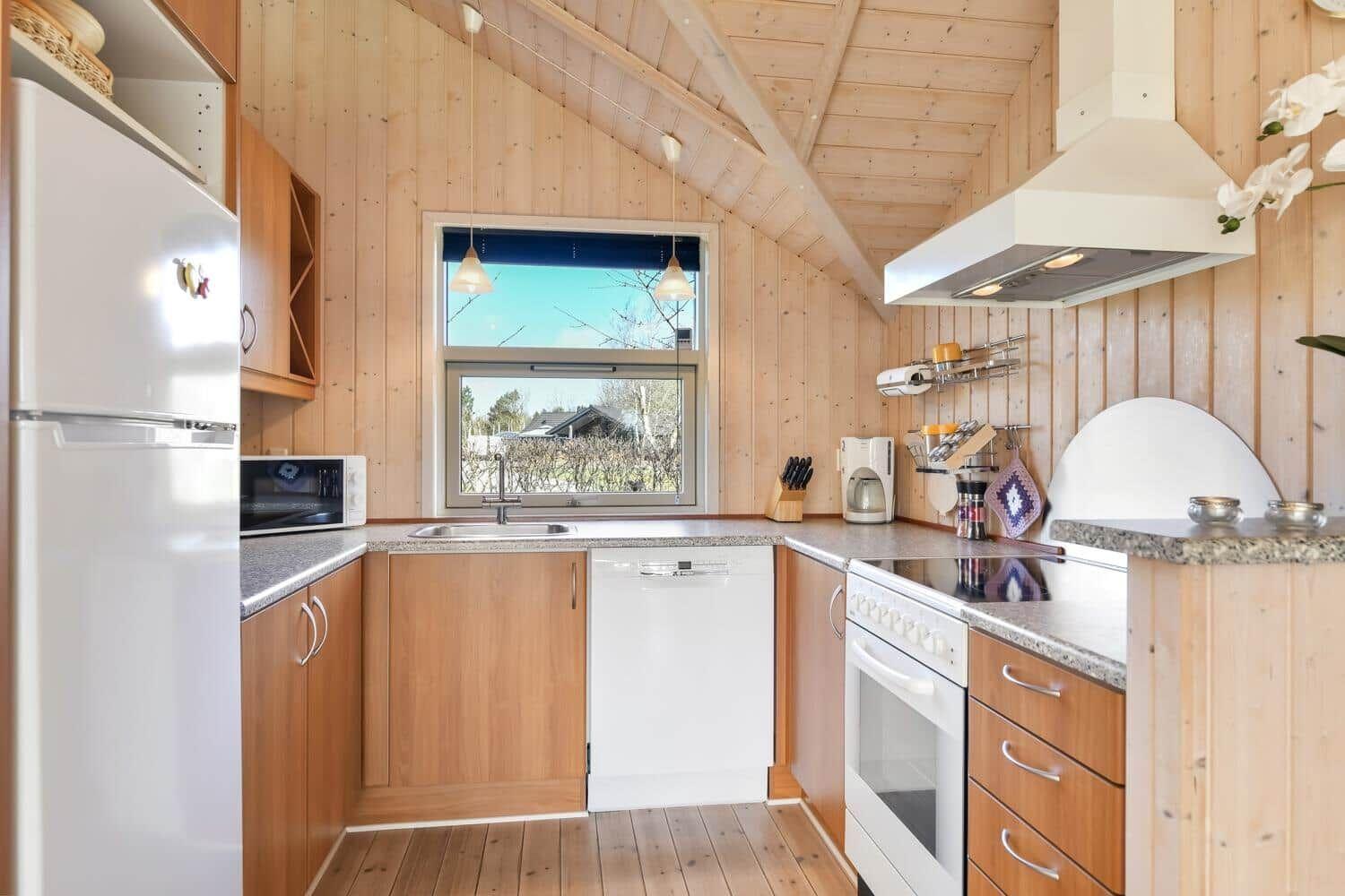 Küche mit Holzwänden, weißen Geräten und Fenster mit Blick nach draußen.