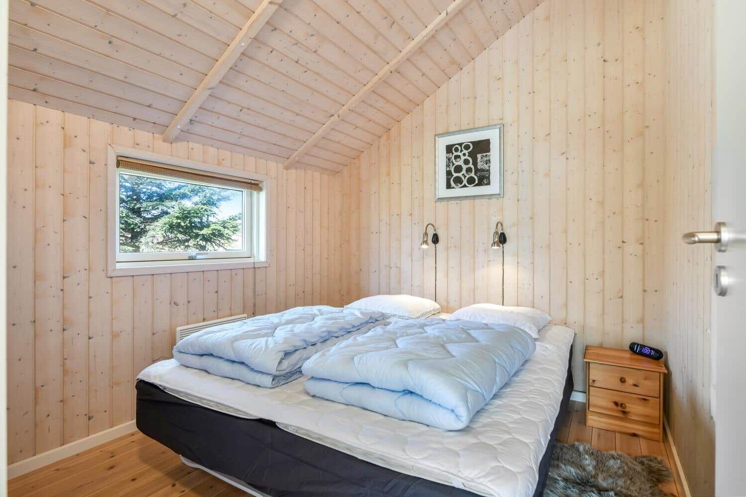 Schlafzimmer mit Holzwand, Bett und Fenster mit Blick auf Bäume