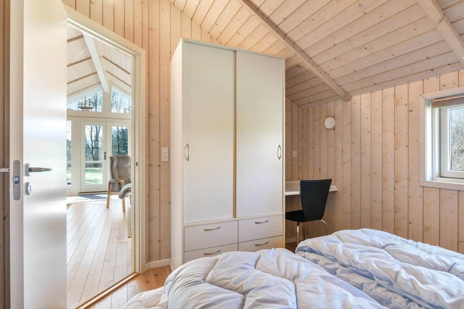 Schlafzimmer mit Bett, Kleiderschrank und Schreibtisch. Durchgang zu Wohnbereich mit Fenster.