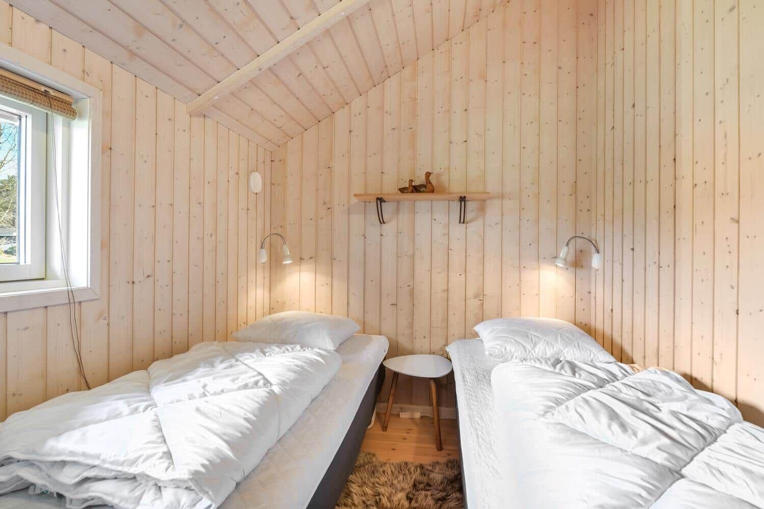 Zwei Betten mit weißen Bettwäsche, Holzwände und kleiner Tisch.