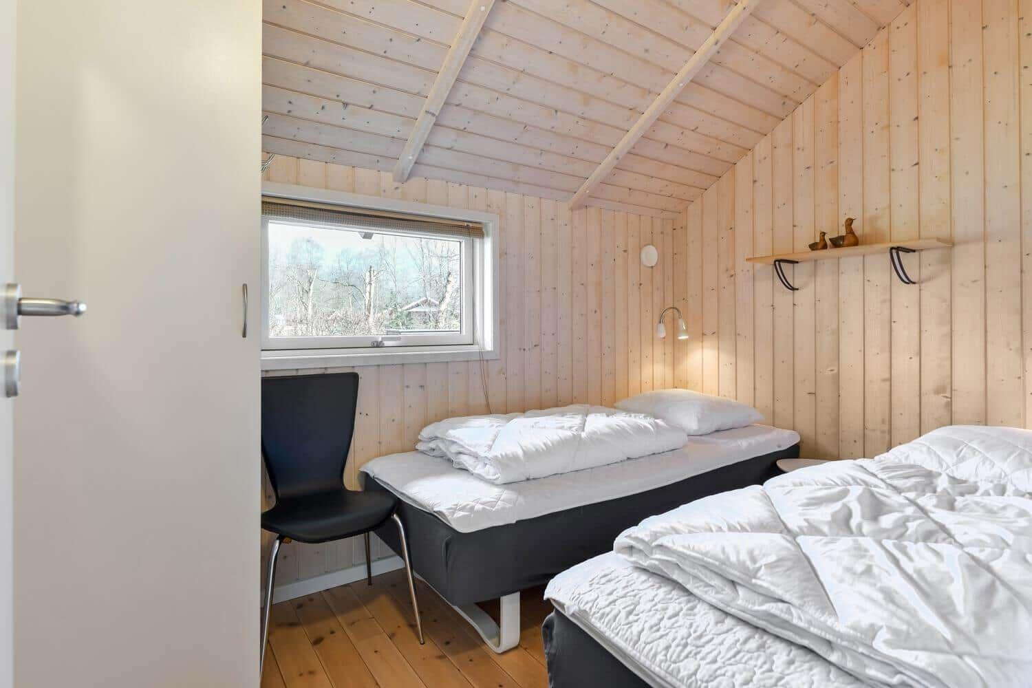 Zwei Betten, Fenster mit Blick, Holzwand und Stuhl im Zimmer.