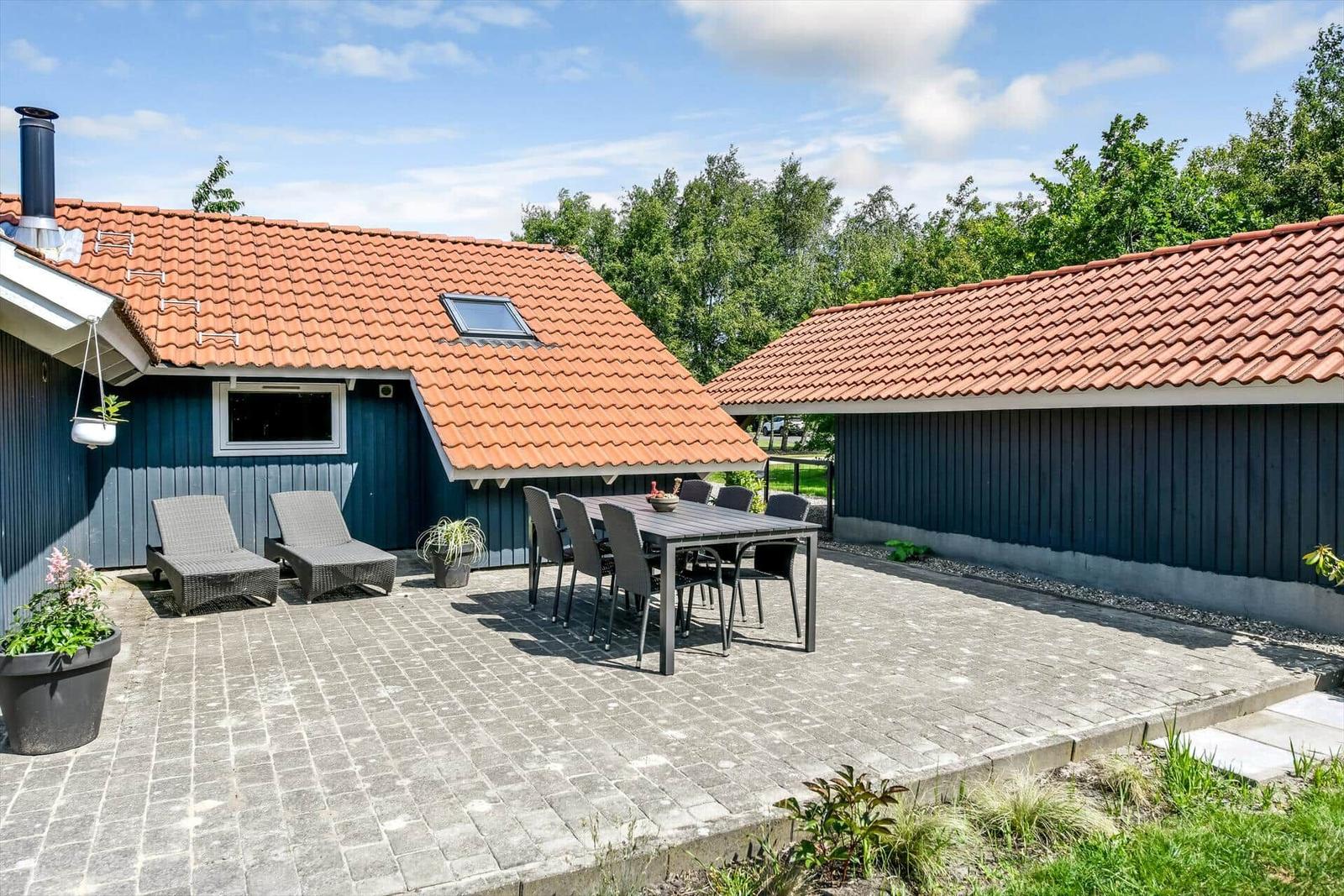 Terrasse mit Tisch, Stühlen und Liegestühlen vor blauem Haus mit rotem Dach.