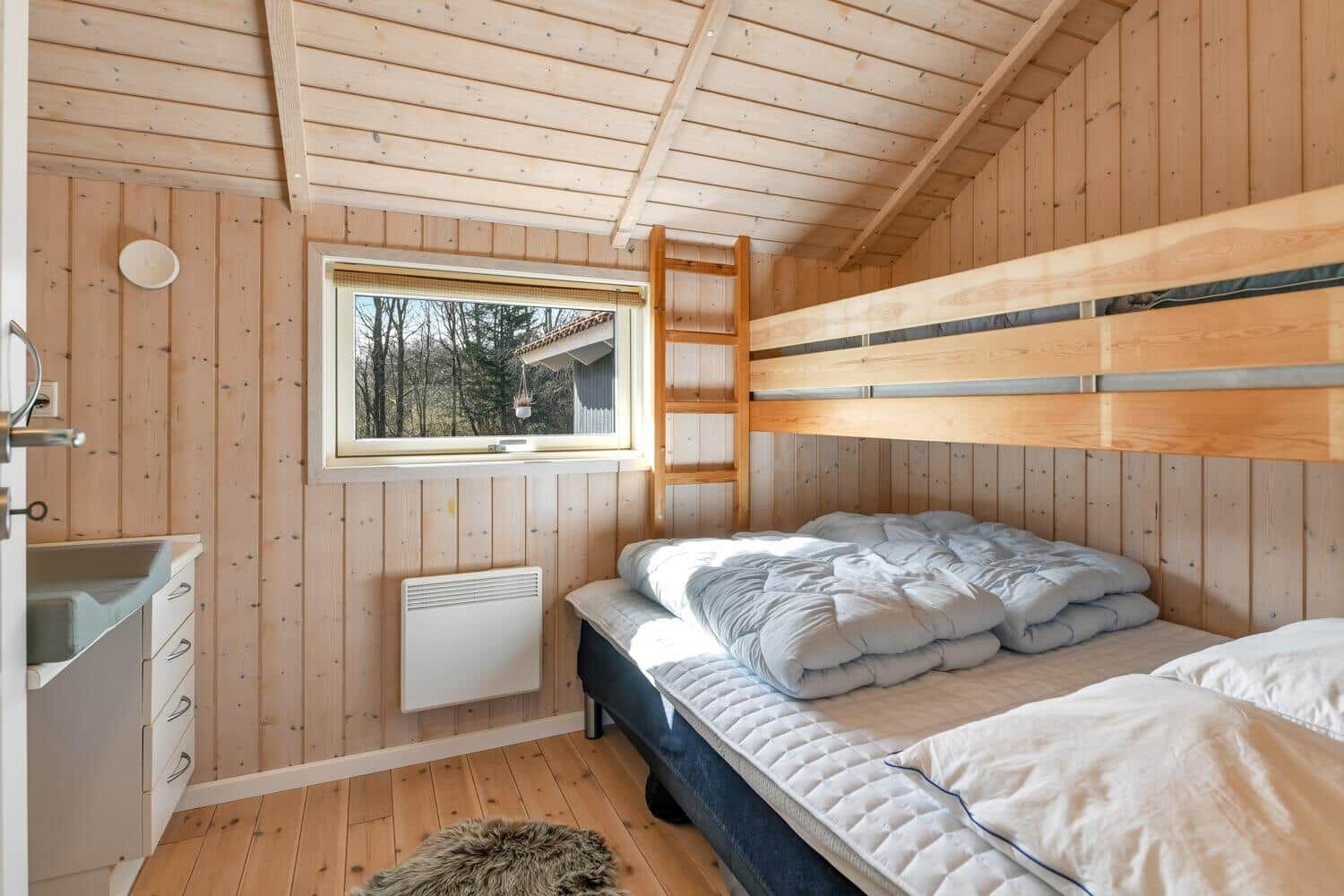 Zimmer mit Holzwand, Doppelbett und Fenster mit Blick auf Wald.