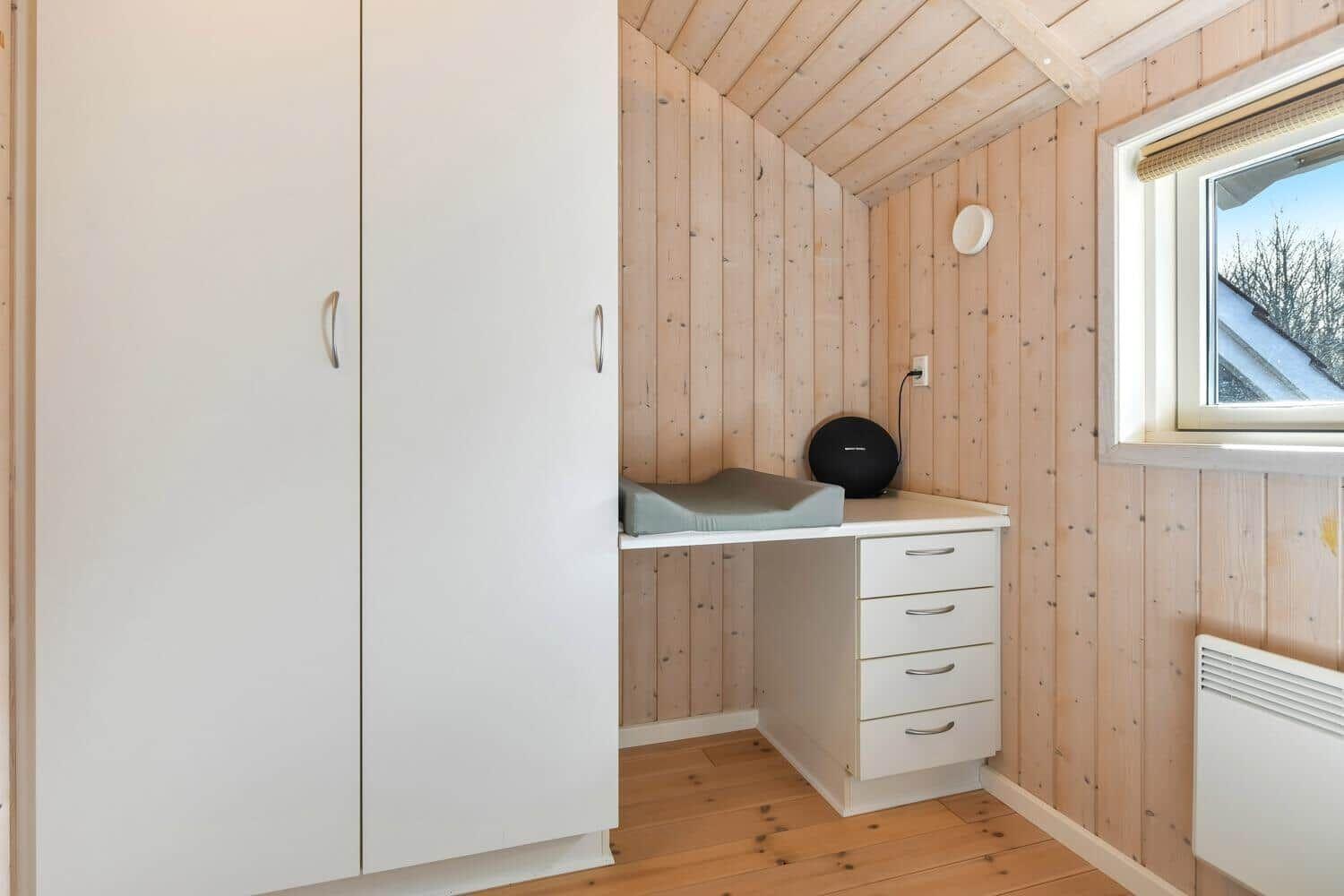 Schlafzimmer mit weißen Schränken und Holzwänden. Fenster und Heizkörper sind sichtbar.