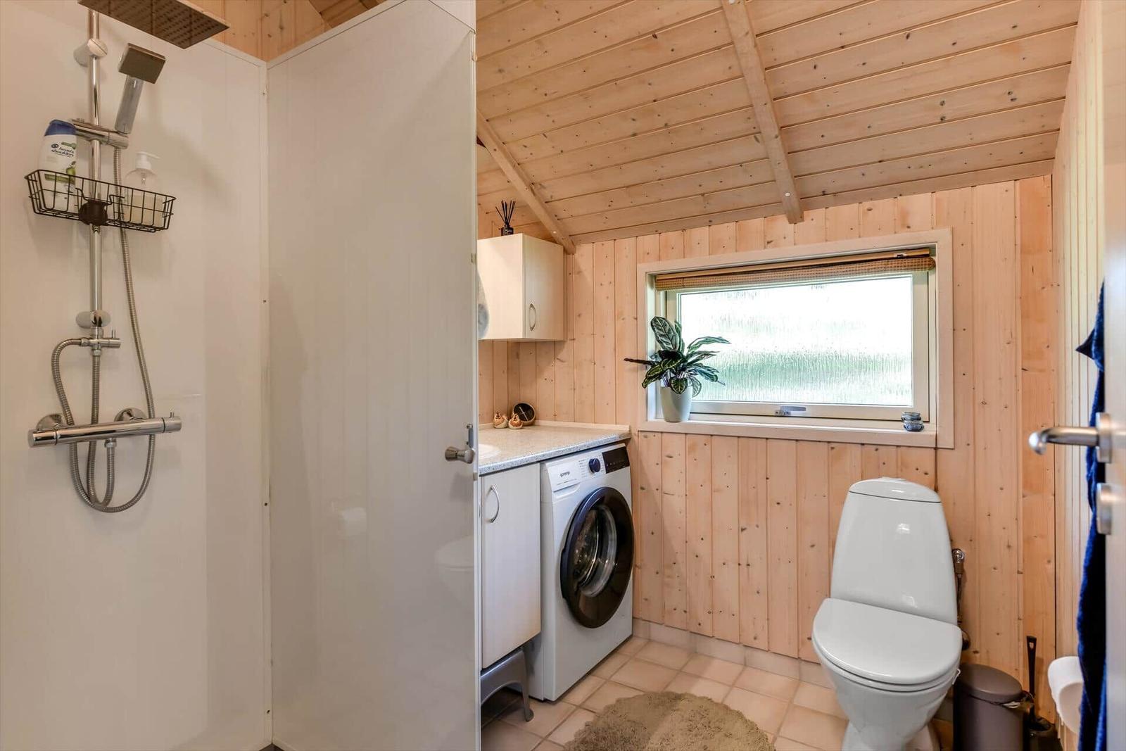 Badezimmer mit Dusche, Waschmaschine und Toilette. Holzwand und Fenster.