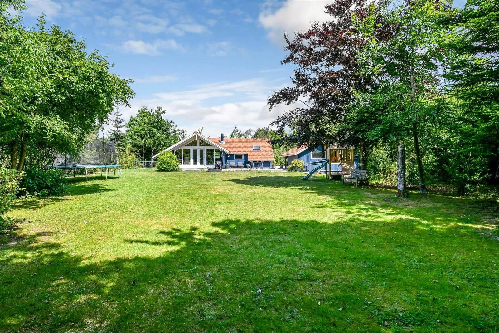 Ein Haus mit großem Garten, Trampolin und Spielplatz unter Bäumen.