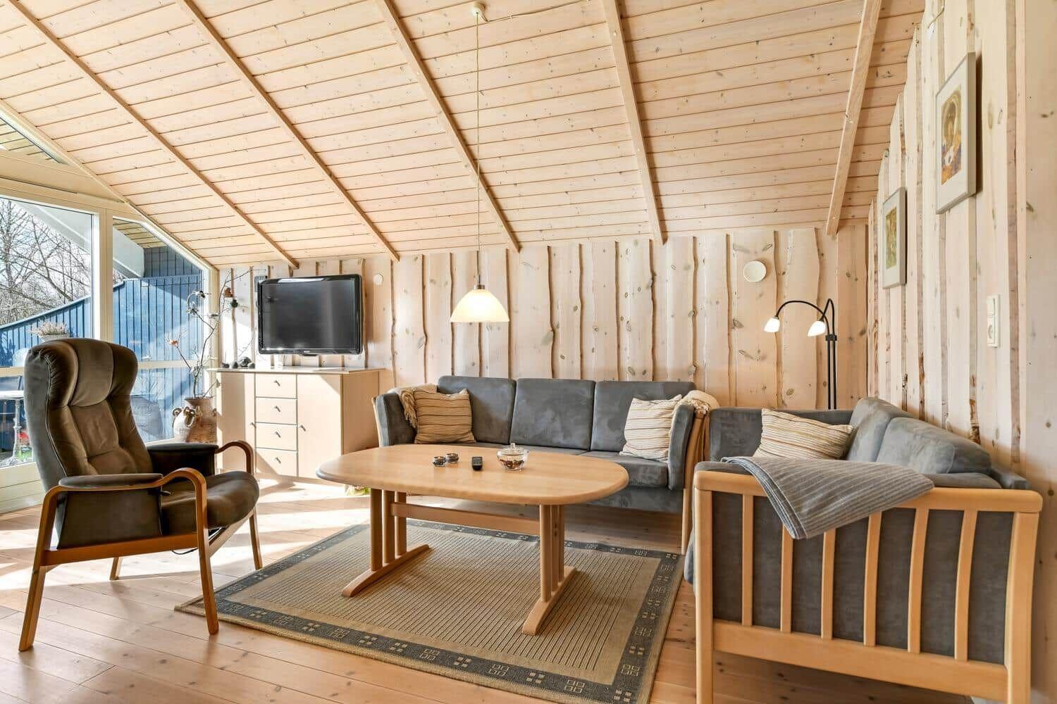 Wohnzimmer mit Holzwand, Sofa, Sessel und Couchtisch.