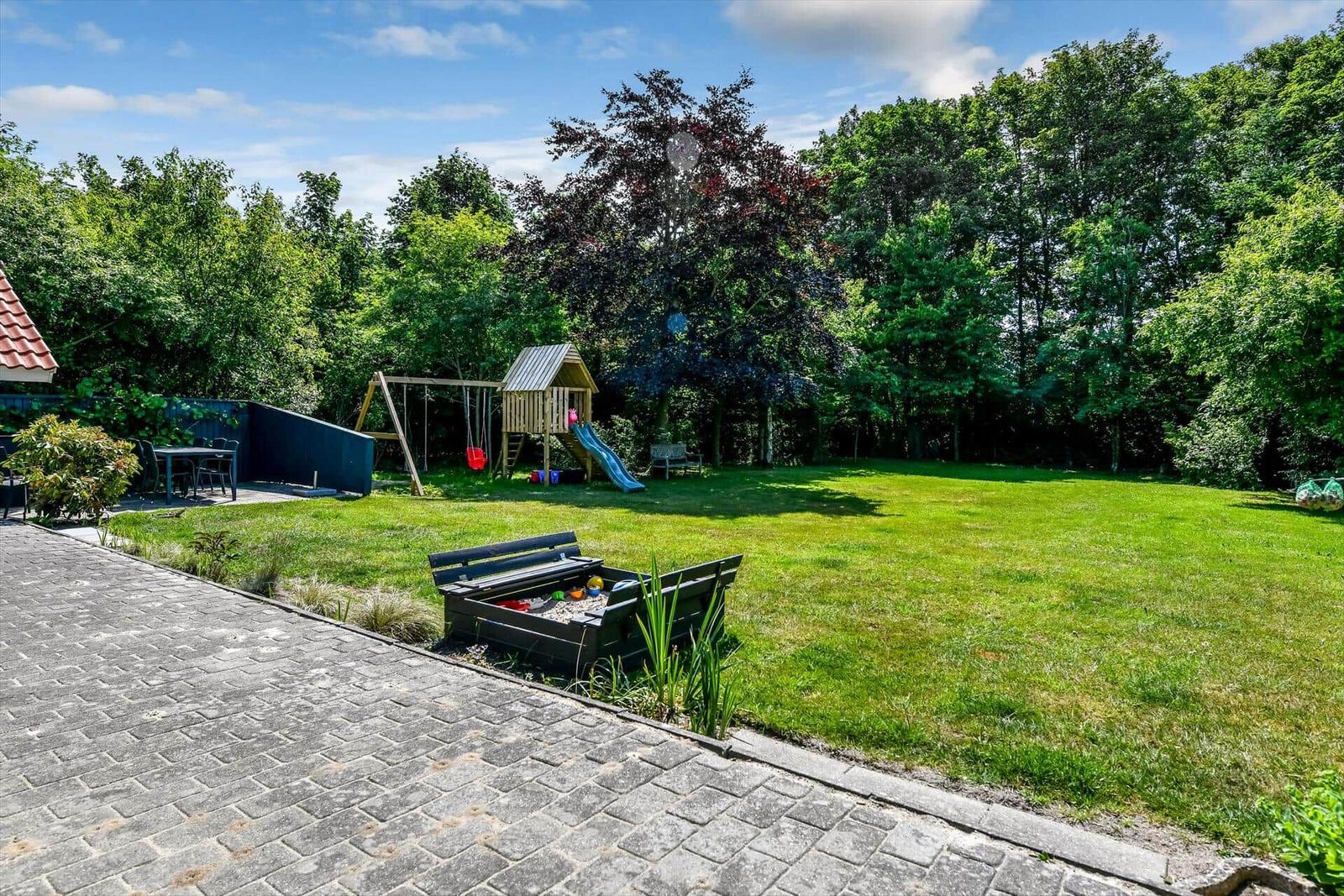 Grüner Garten mit Spielplatz, Sandkasten und Terrasse. Umgeben von Bäumen.