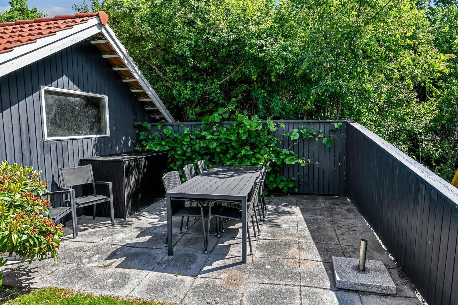 Terrasse mit Tisch und Stühlen neben einem grauen Haus mit rotem Dach.