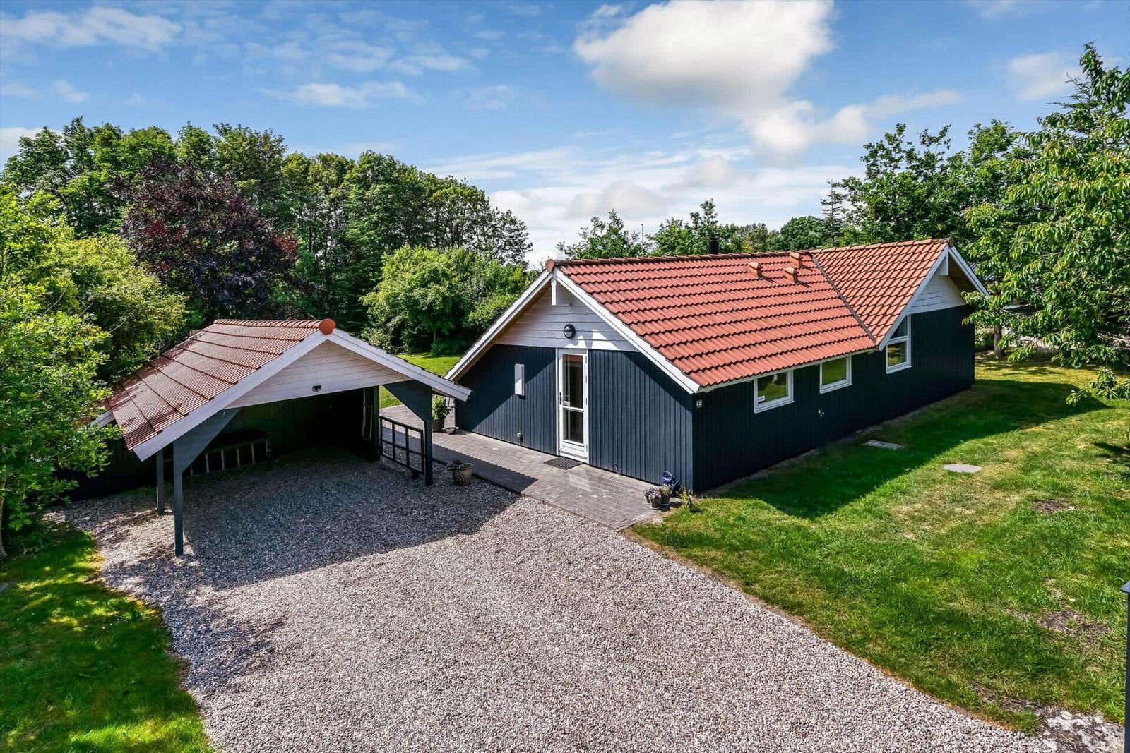 Schwarzes Haus mit rotem Dach und Carport auf grünem Grund.