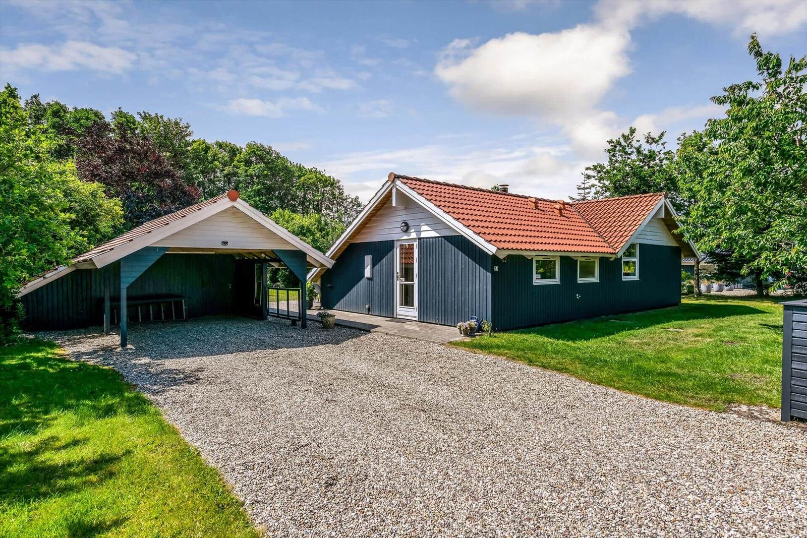 Ein dunkelblauer Ferienhaus mit rotem Dach und Carport auf grünem Grund.