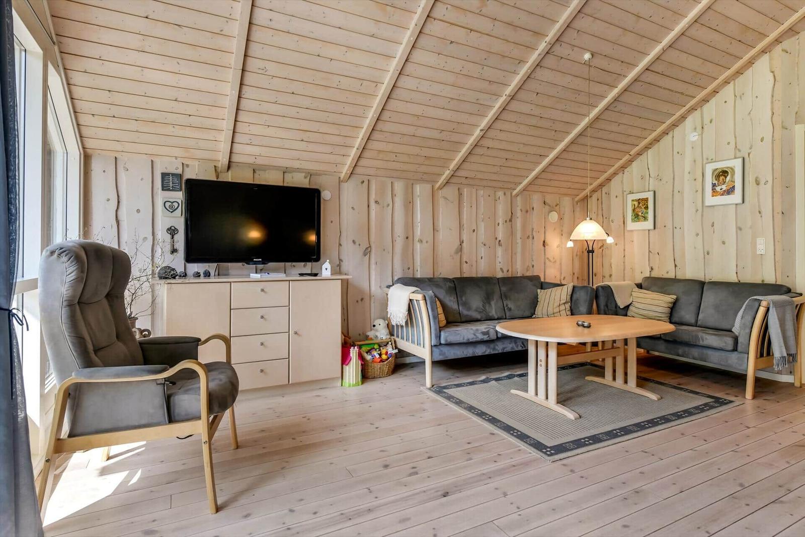 Wohnzimmer mit Holzwand, Sofa, Sessel und Fernseher.