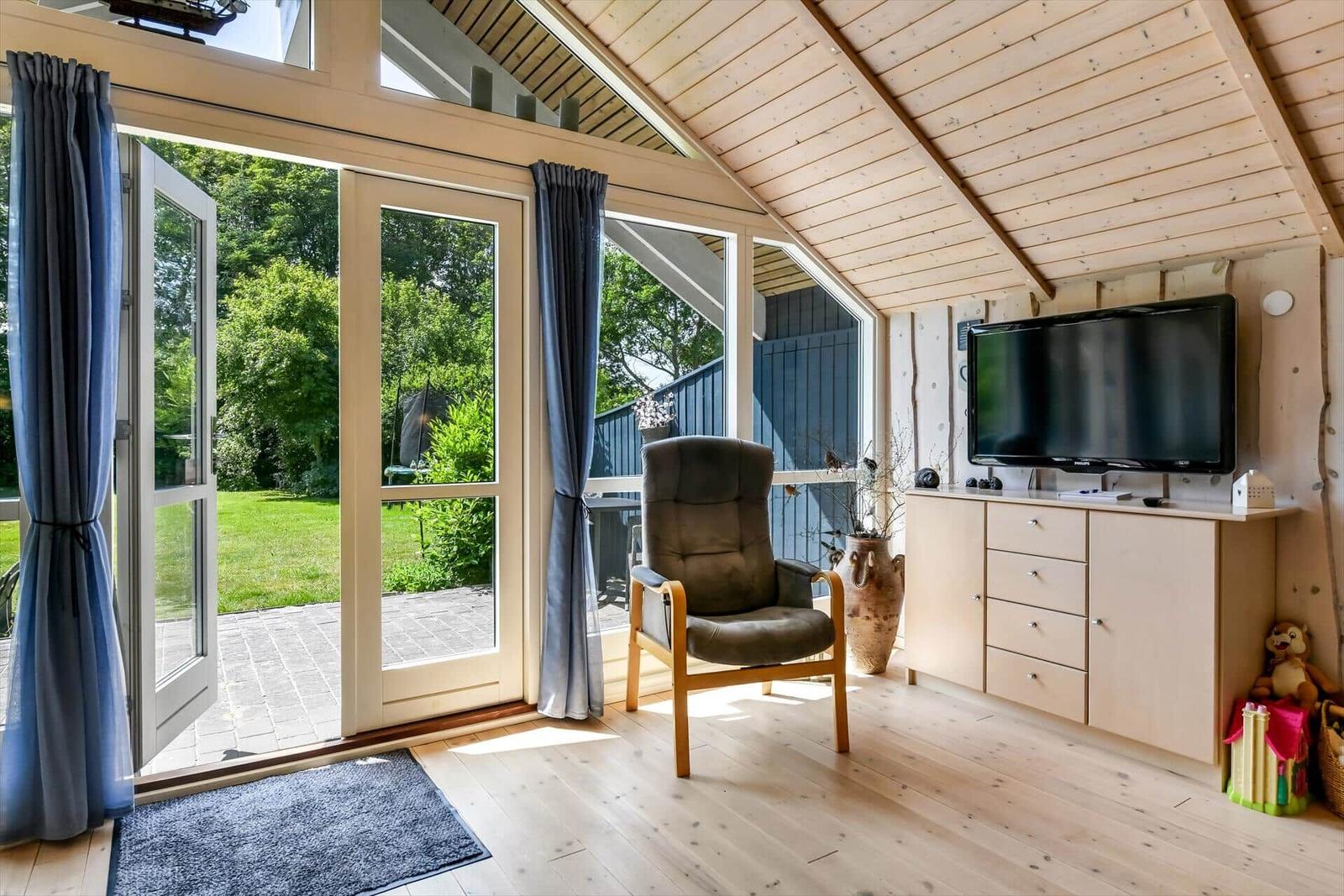 Raum mit Sessel, TV und Blick auf Garten durch Glastüren.