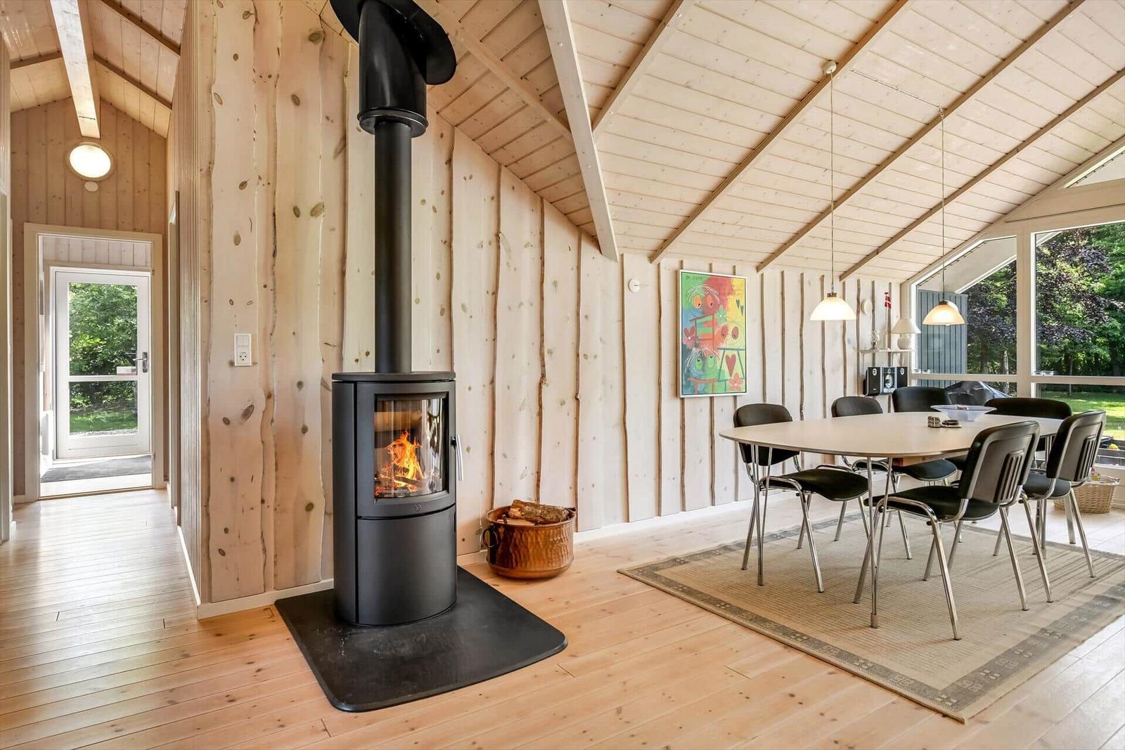 Holzvertäfelte Raum mit Kaminofen, Esstisch und Fenster zur Außenseite.
