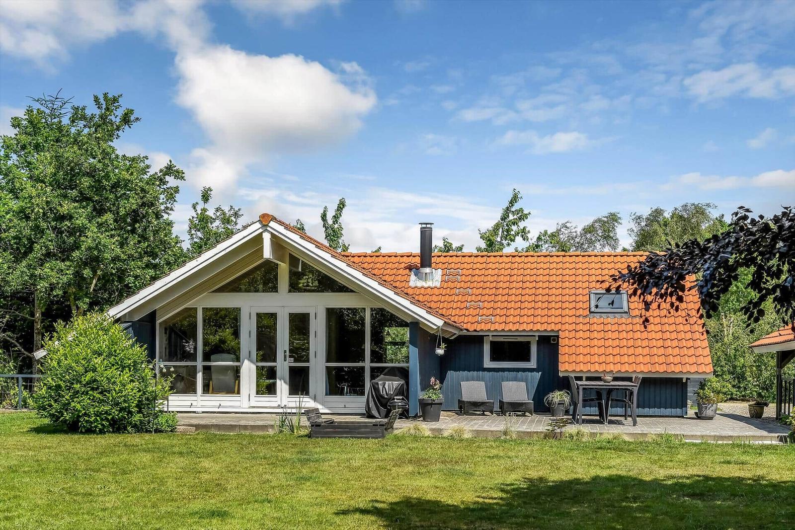 Ein Haus mit rotem Dach und blauen Wänden. Außenbereich mit Tisch, Stühlen und Grill.