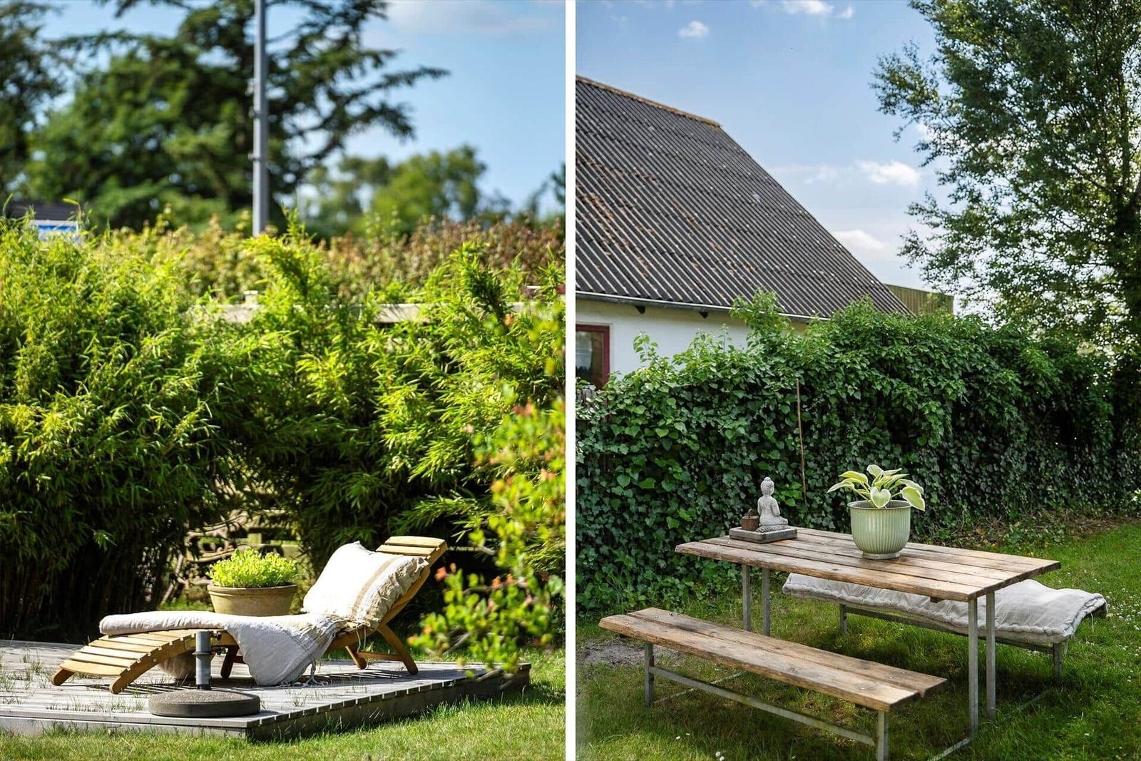 Terrasse mit Liegestuhl und Gartenmöbeln vor grüner Hecke und Haus.