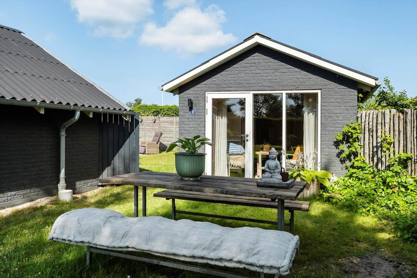 Hinterhof mit Tisch, Bank und Buddha-Statue vor grauem Haus mit Glasfront.