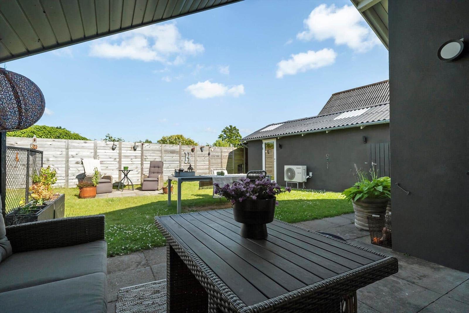 Terrasse mit Tisch, Sitzgelegenheiten und Garten. Hinterhof mit Grill und Pflanzen.