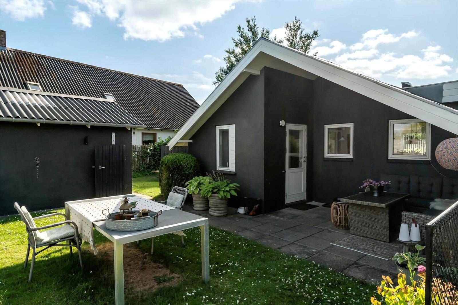 Haus mit Garten, Terrasse und Sitzgelegenheiten unter blauem Himmel.