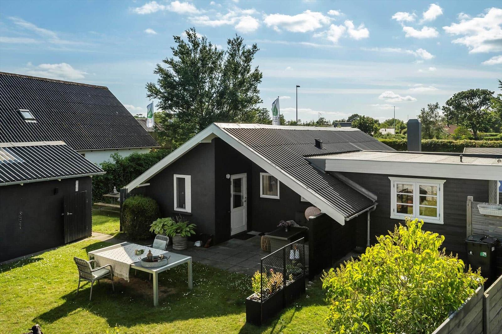 Schwarze Ferienhaus mit Garten und Außentisch unter blauem Himmel.