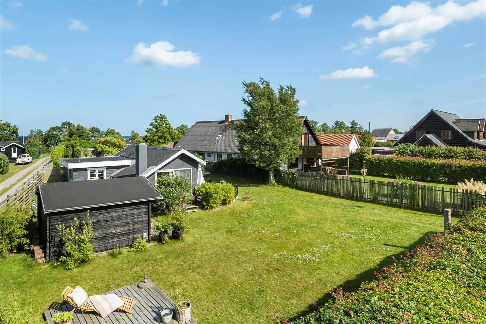 Grüner Garten mit Holzterrasse und Blick auf mehrere Häuser und Bäume.