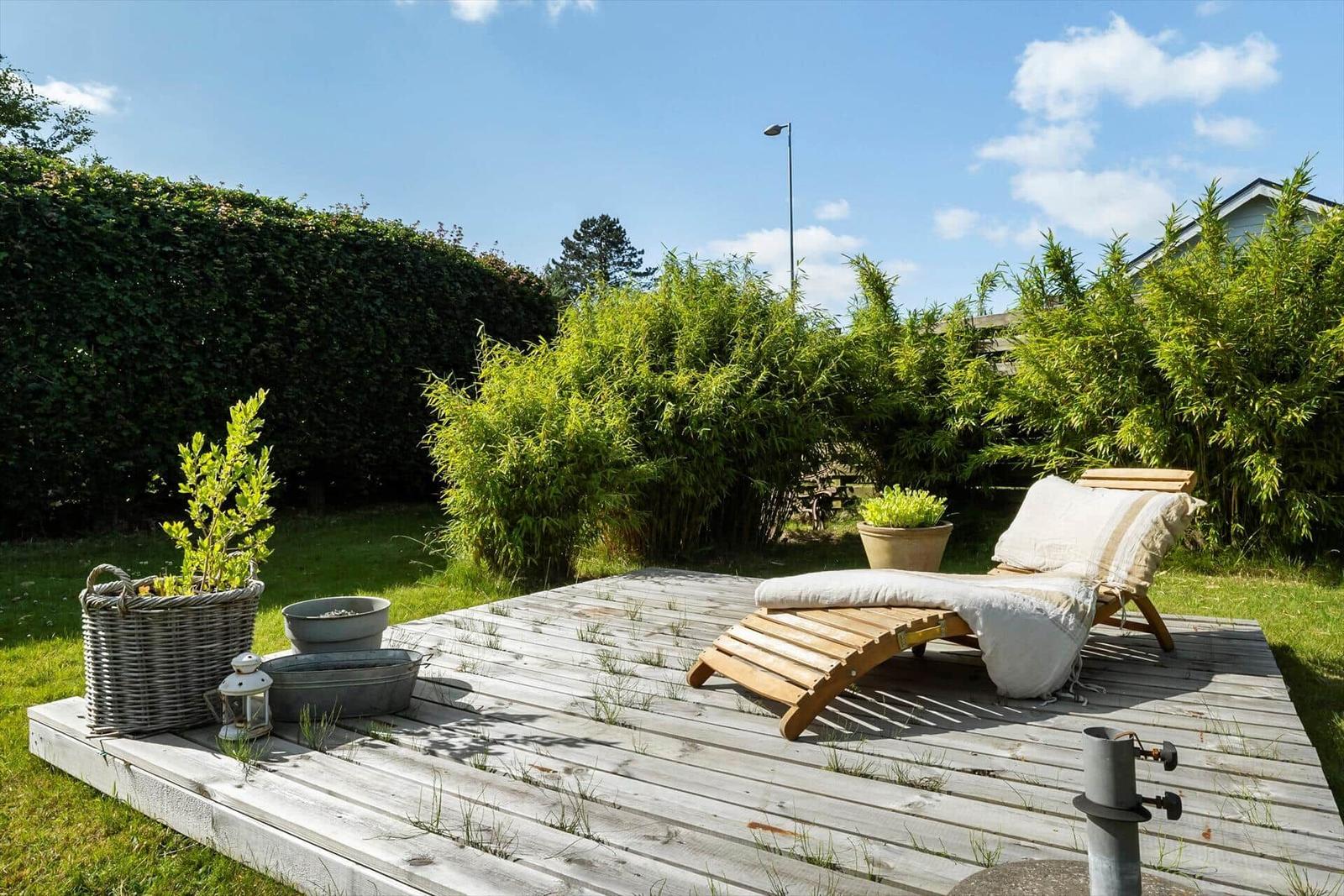 Holzterrasse mit Liegestuhl, Pflanzen und Gartenmöbeln.