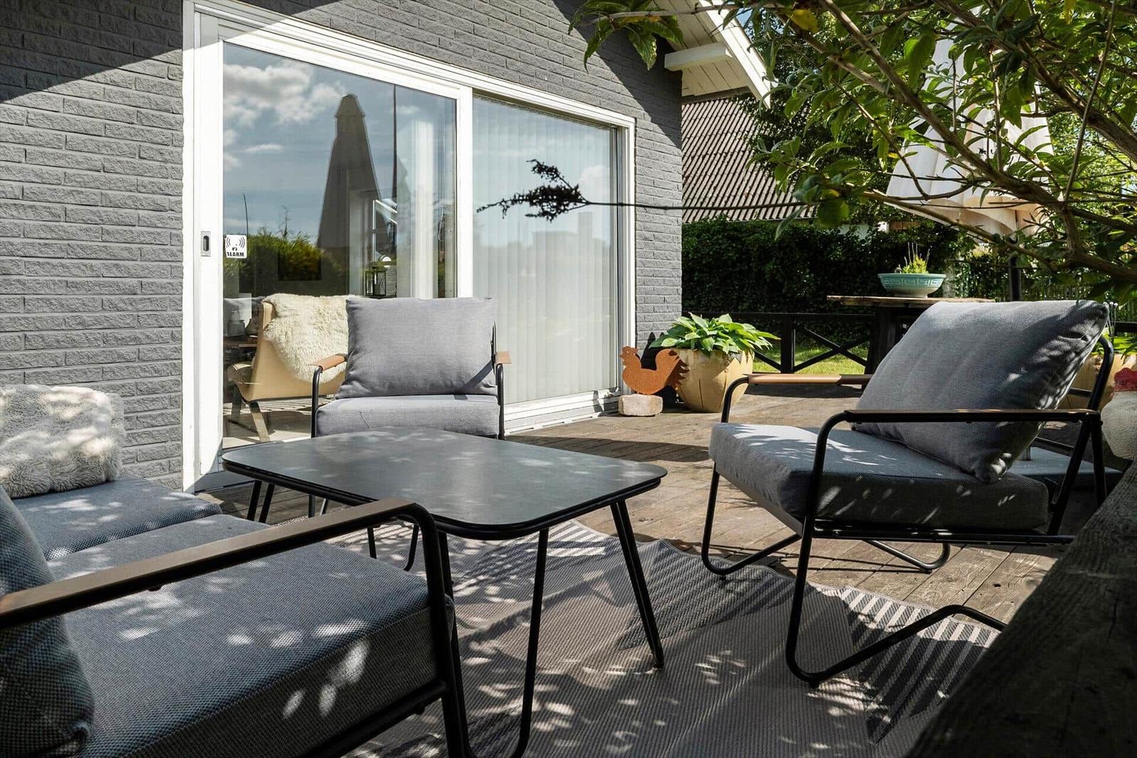 Terrasse mit Sitzgruppe, Tisch und Pflanzen vor grauem Backsteinhaus.