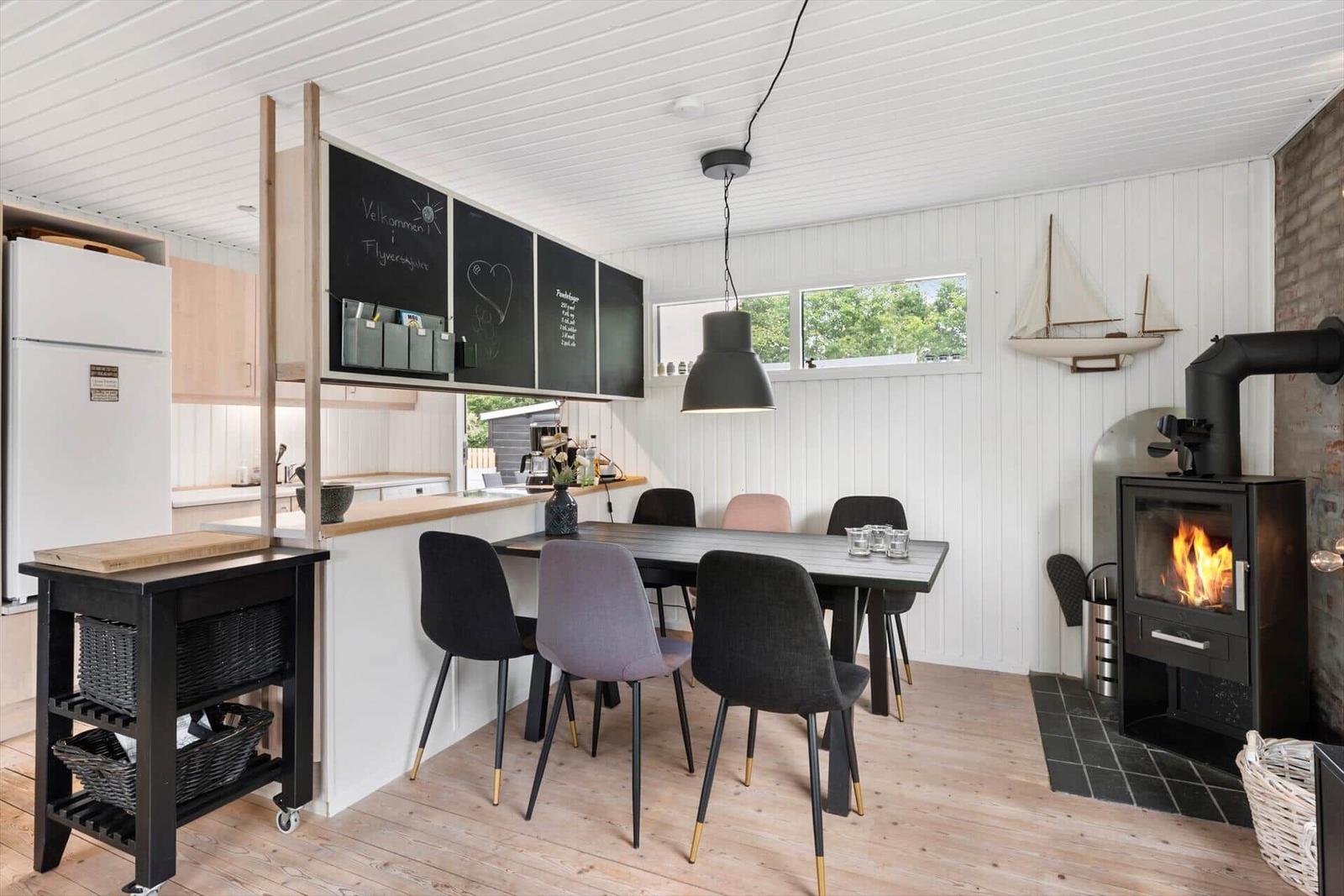 Essbereich mit Tisch, Stühlen und Kaminofen. Küche mit Kühlschrank und Schieferwand.