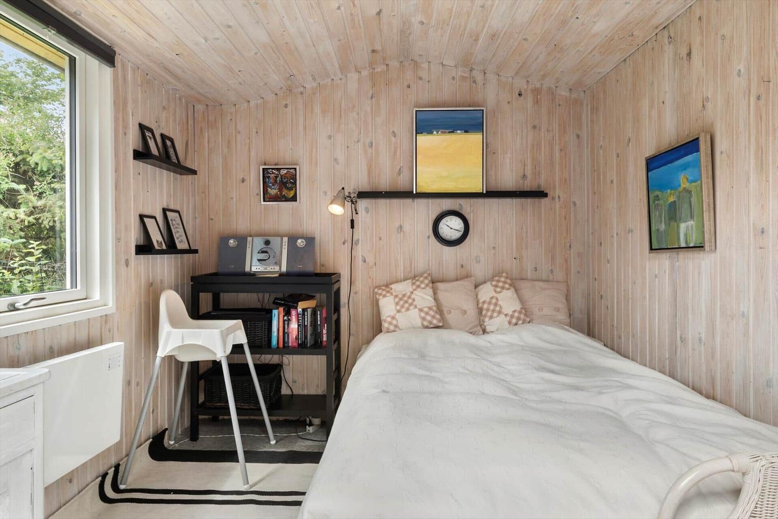Schlafzimmer mit Holzwand, Bett, Schreibtisch und Fenster.