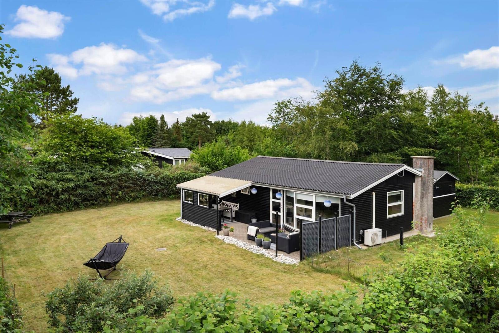 Schwarzes Ferienhaus mit Terrasse und Garten unter blauem Himmel.