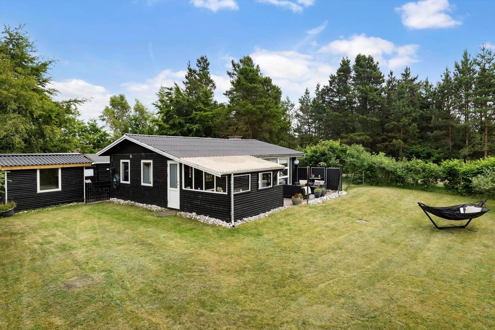 Schwarzes Holzhaus mit Garten, Sonnenschutz und Hängematte.