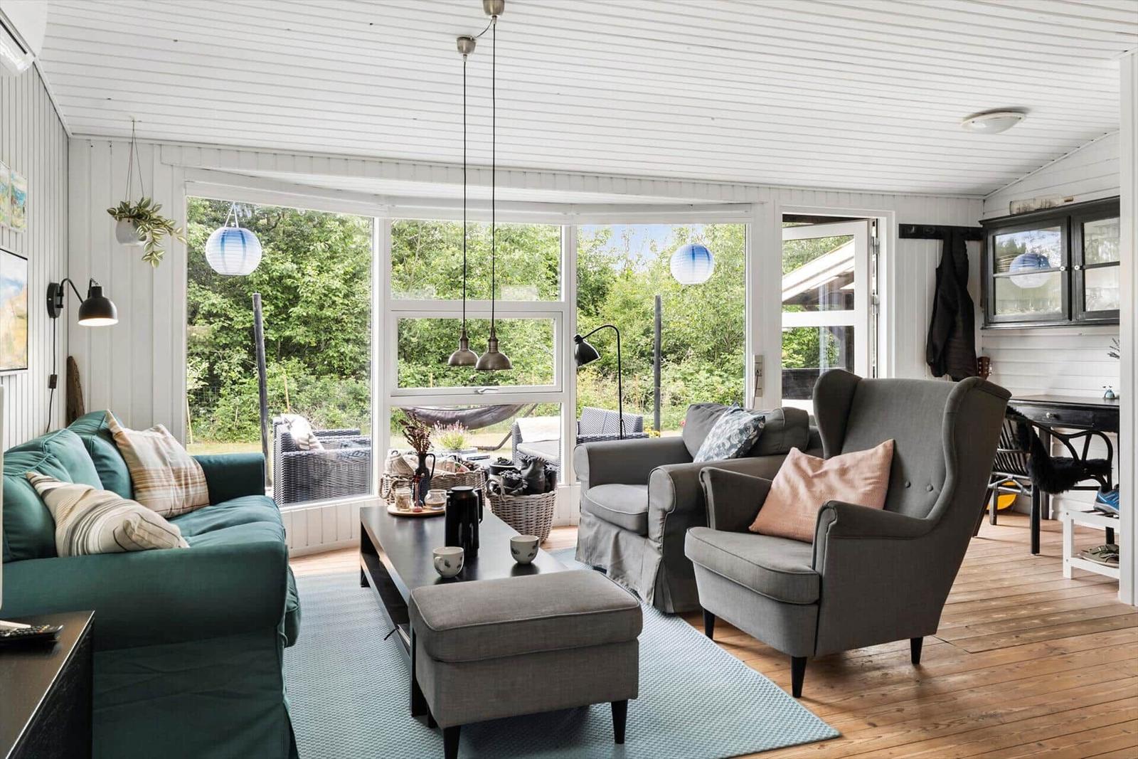 Wohnzimmer mit Sofa, Sesseln und großem Fenster. Holzboden und helle Wände.