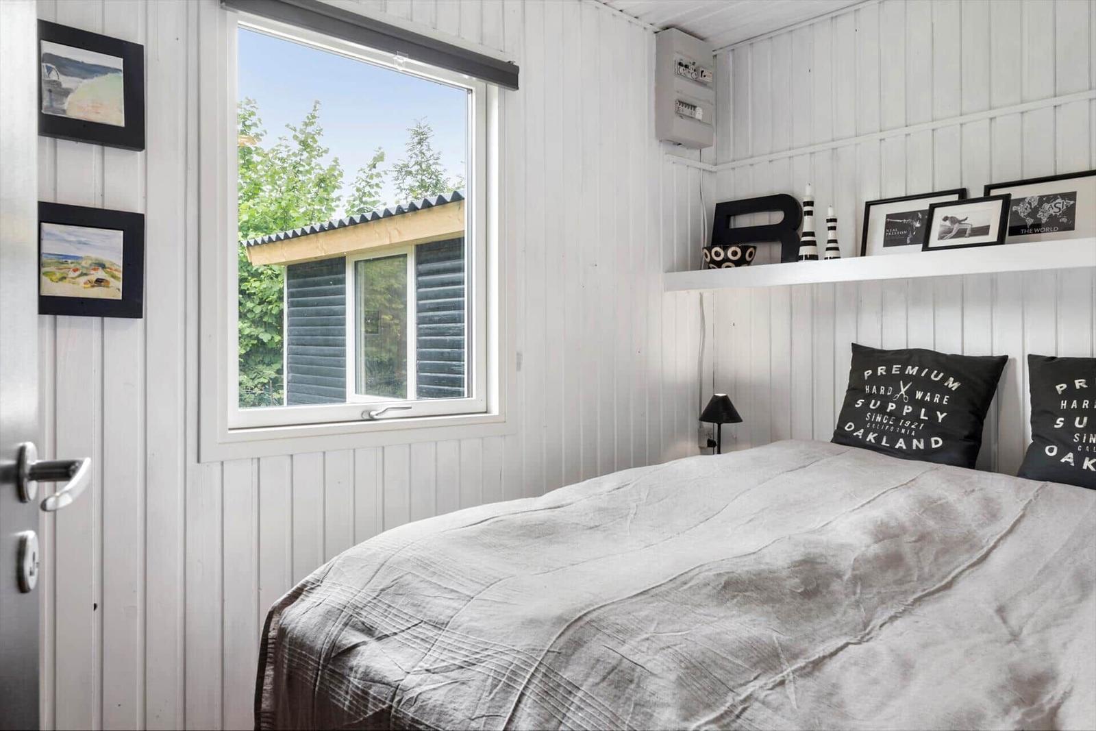 Schlafzimmer mit Bett, Fenster und Wandregal mit Dekoration.