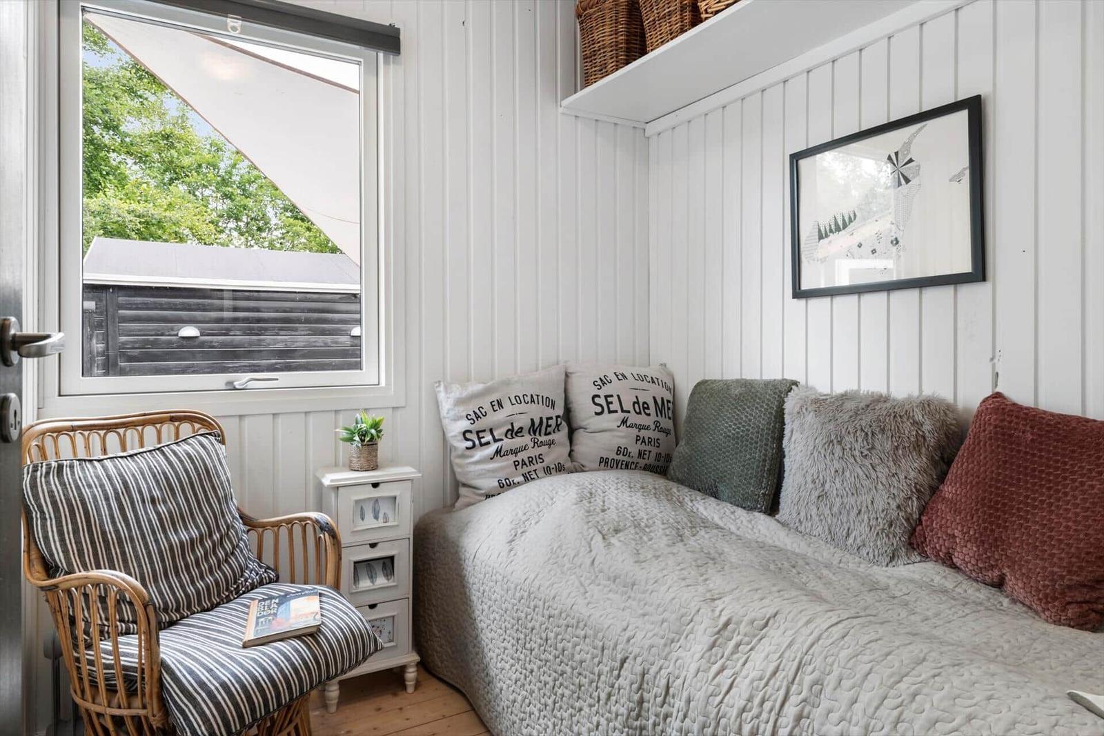 Schlafzimmer mit Bett, Stuhl und Fensterblick auf Holzhaus