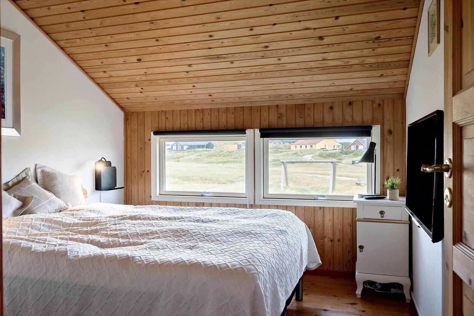 Schlafzimmer mit Doppelbett, Holzdecke und Blick auf Felder.