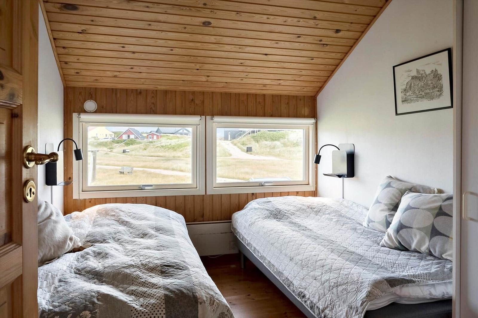 Zwei Betten mit Blick auf Grünflächen und Häuser. Holzdecke und Wandverkleidung.