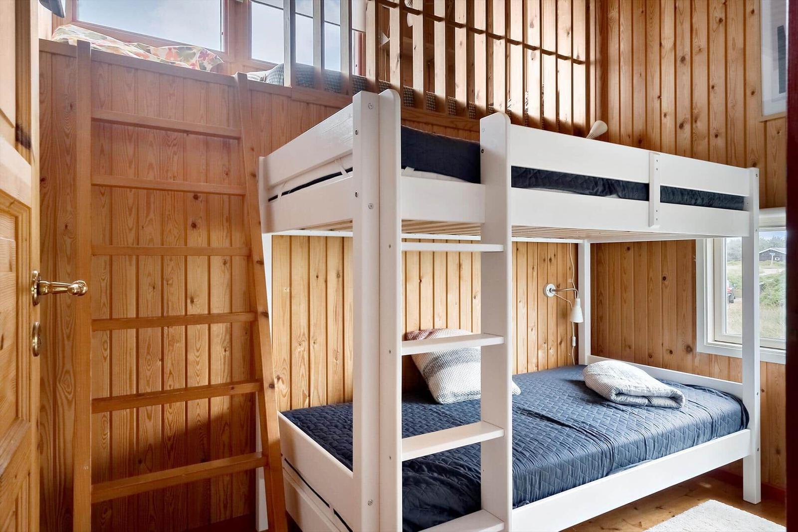 Zimmer mit weißem Doppelstockbett und Holzwänden. Fenster und Tür sichtbar.