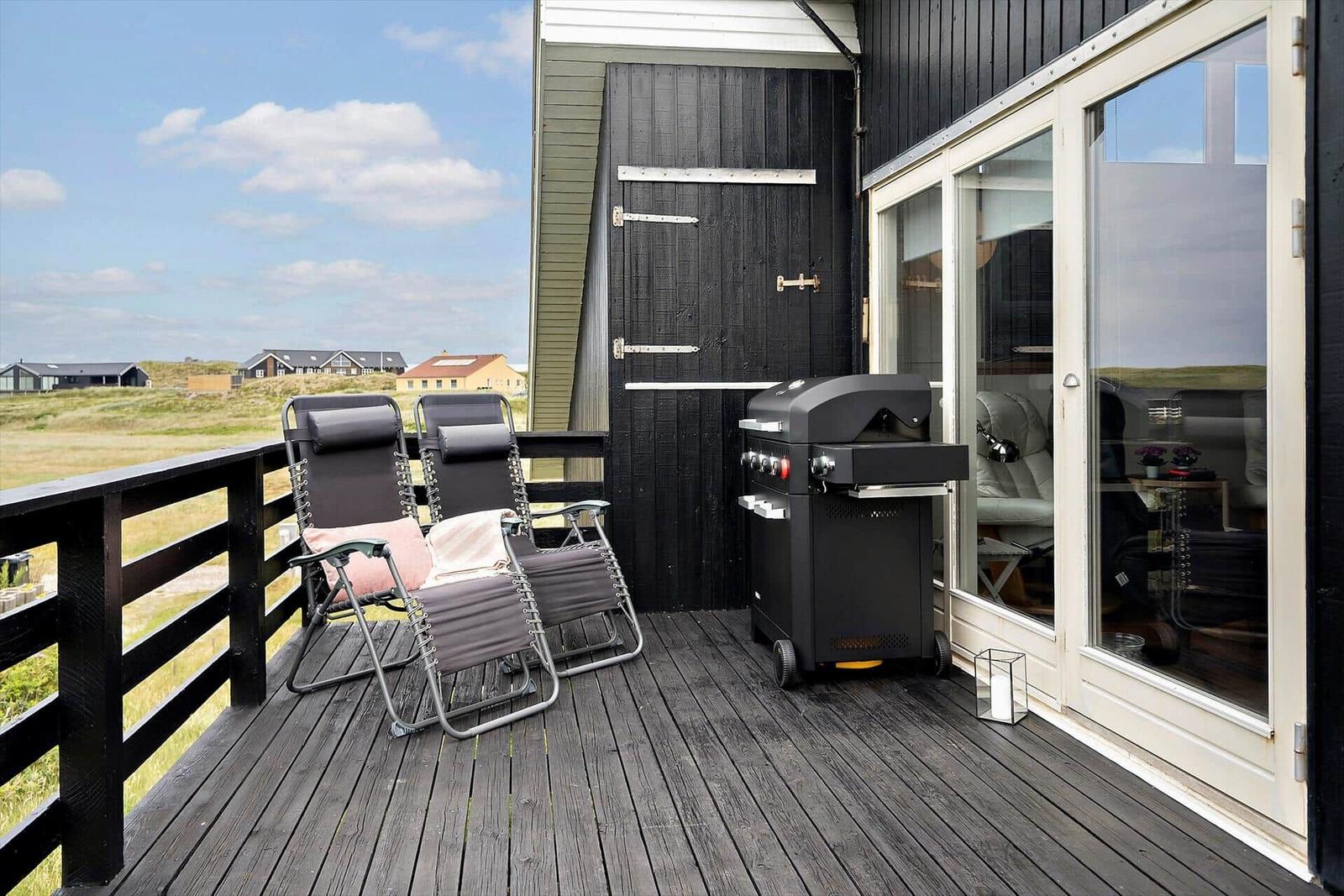 Terrasse mit zwei Liegestühlen und Grill, Blick auf Grasland und Häuser.