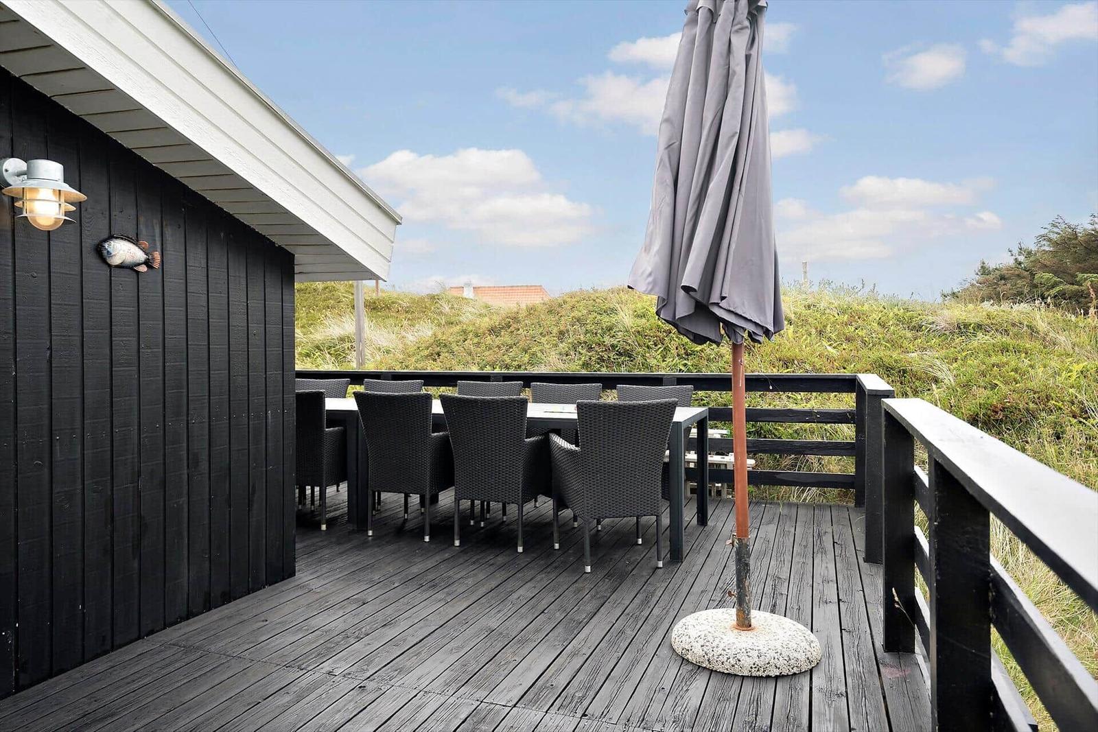 Terrasse mit Tisch, Stühlen und Schirm. Blick auf Gras- und Hügellandschaft.