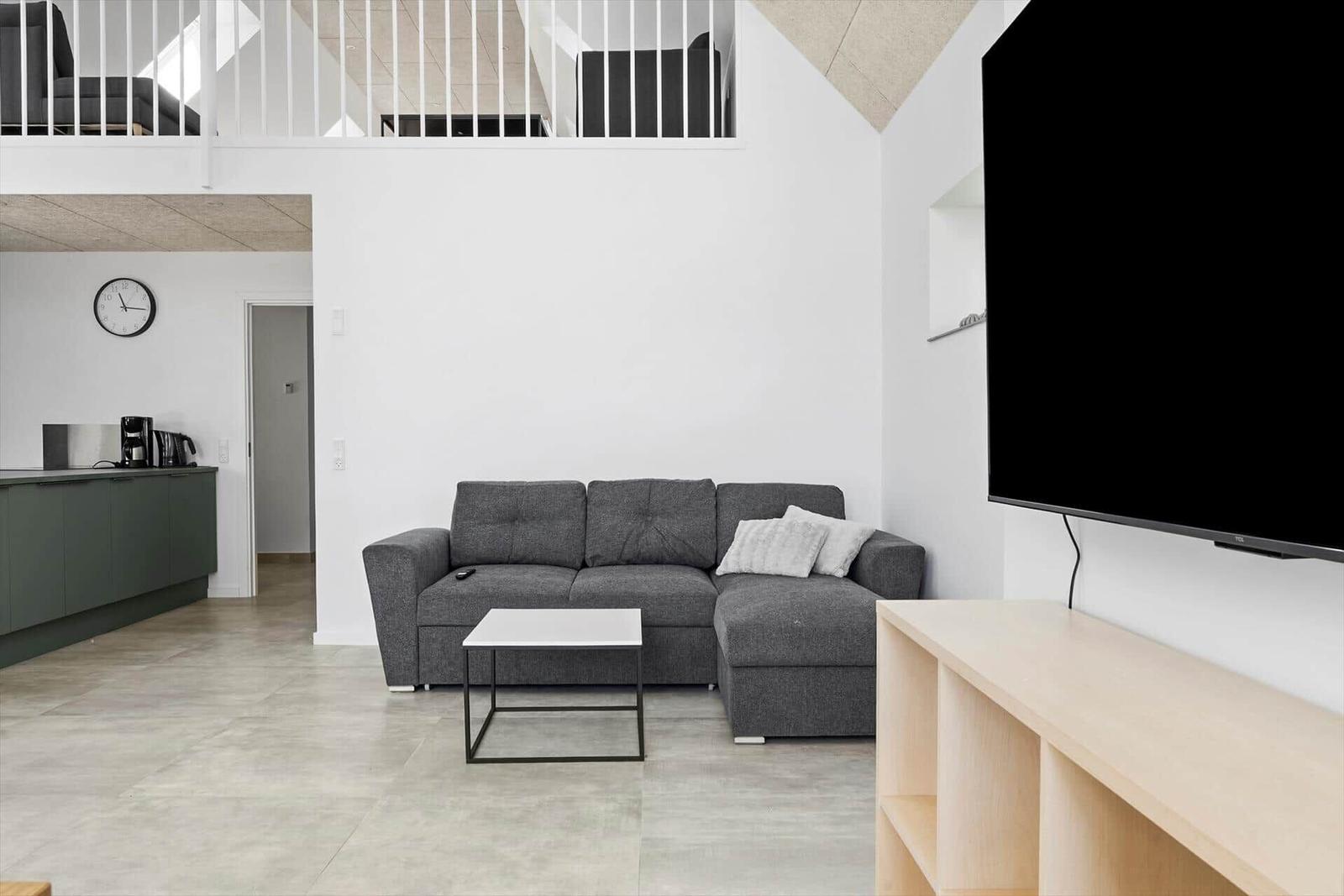 Wohnzimmer mit grauem Sofa, TV und Blick auf die Küche.