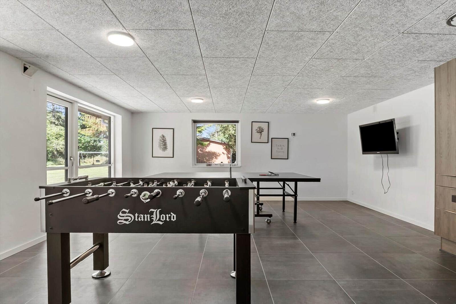 Raum mit Tischfußball und Tischtennisplatte, Wandfernseher und Fenster.
