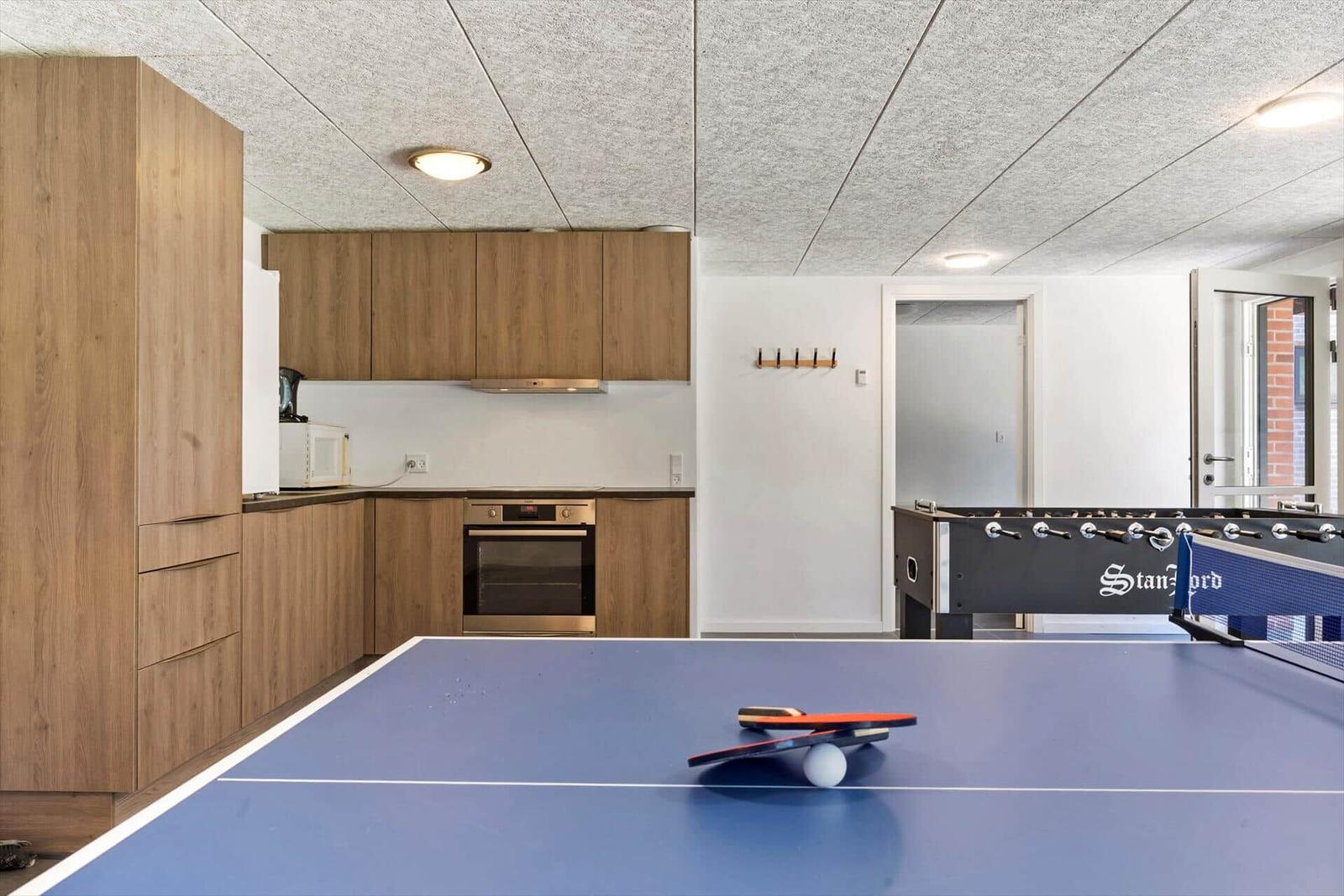 Küche mit Holzschränken und Spielbereich mit Tischtennis- und Fussballtisch.