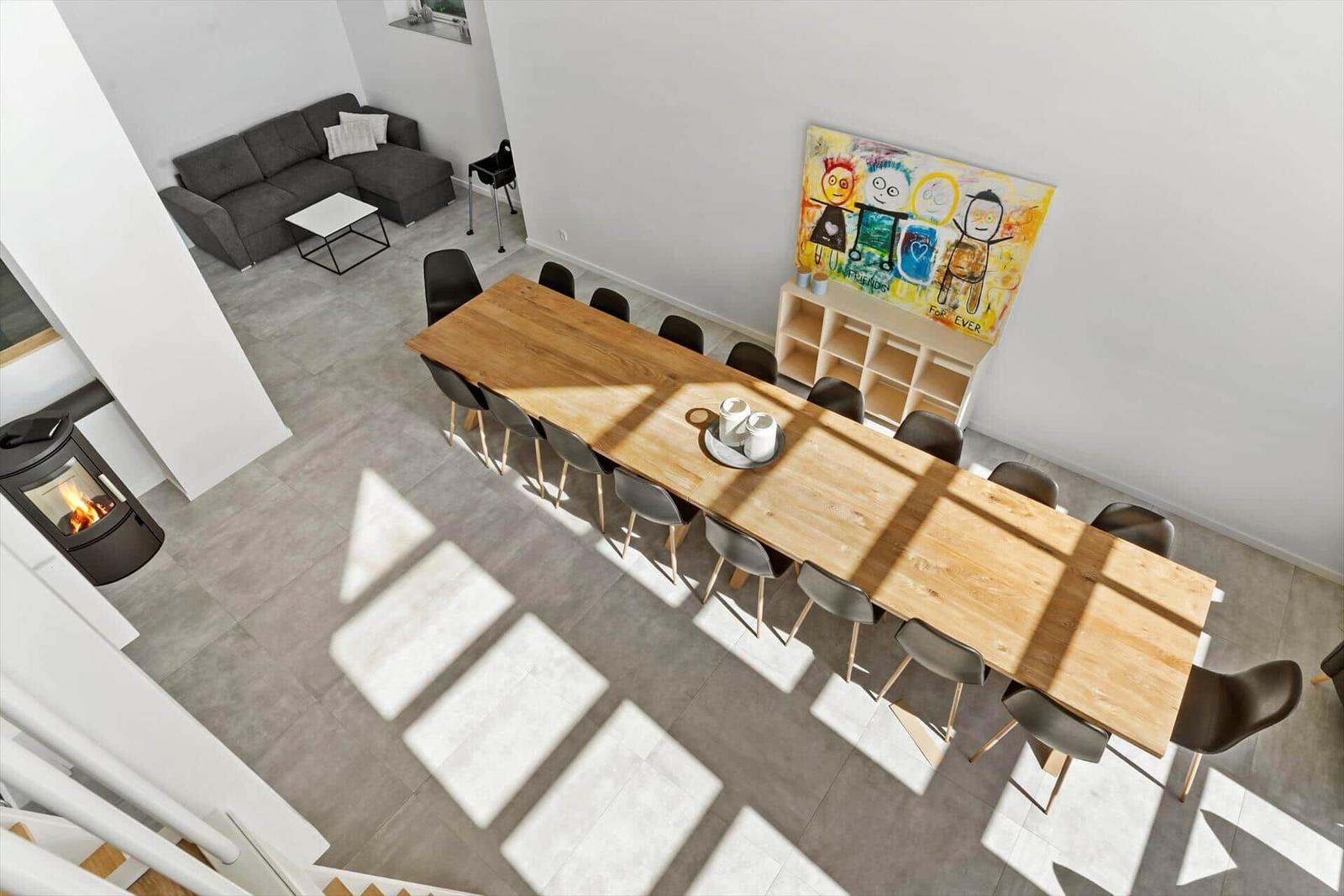 Großer Essbereich mit Holztisch und Stühlen. Im Hintergrund Wohnbereich mit Sofa und Kamin.