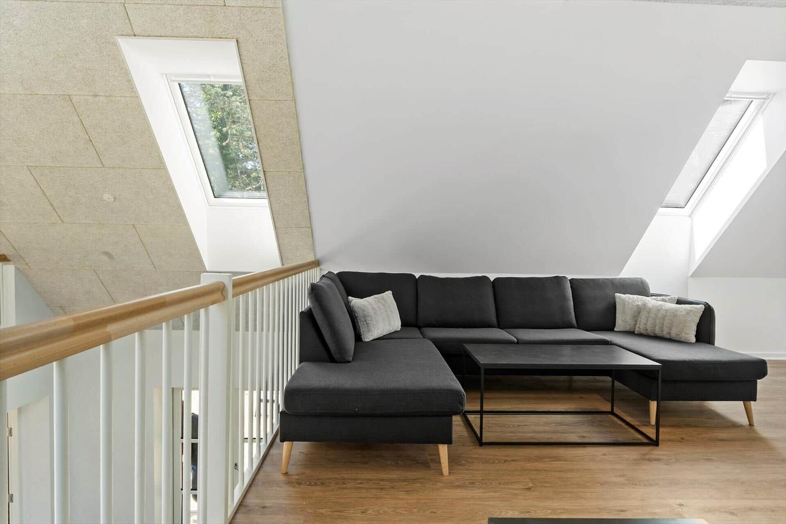 Ein Wohnzimmer mit einem schwarzen Ecksofa, einem Tisch und zwei Dachfenstern.