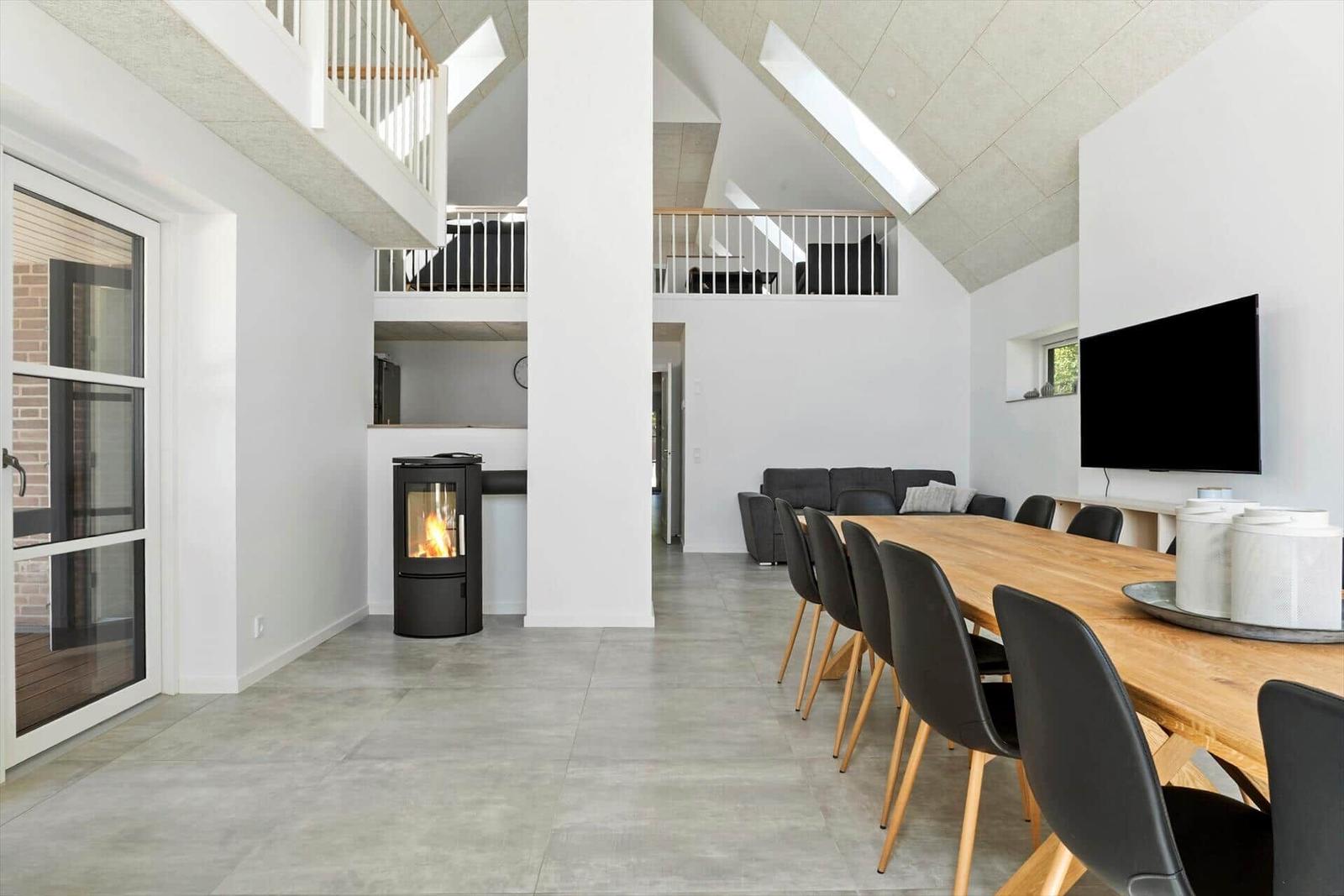 Großer Essbereich mit Holztisch, schwarzen Stühlen und Kaminofen. Obergeschoss mit Balkon.