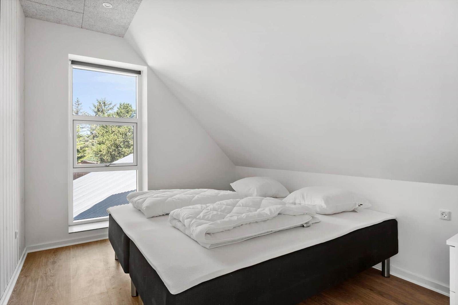 Schlafzimmer mit Dachschrägen, Bett und Fenster mit Blick auf Bäume.