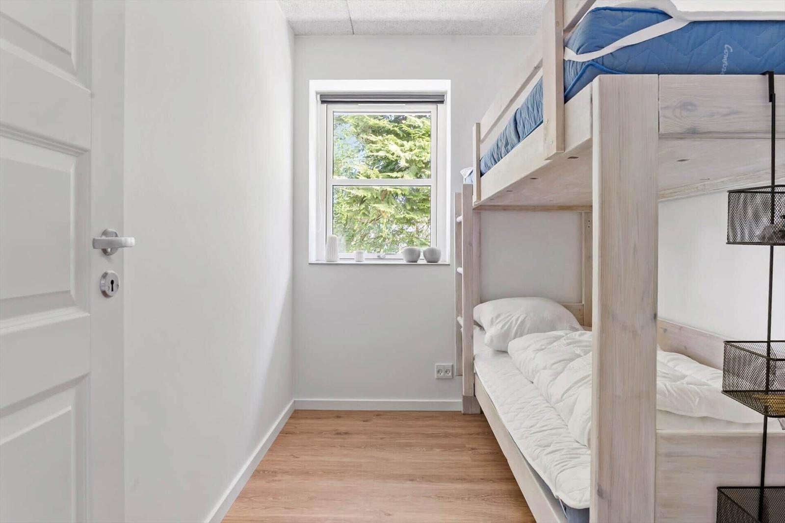 Ein Schlafzimmer mit einem Doppelstockbett und einem Fenster mit Blick auf Bäume.